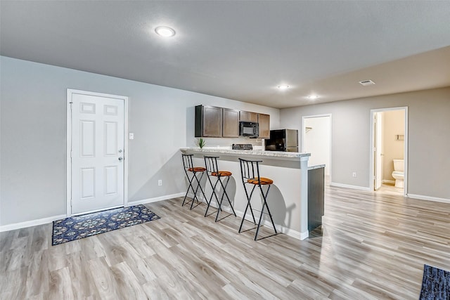 kitchen with black appliances, kitchen peninsula, light wood-type flooring, a breakfast bar area, and dark brown cabinets