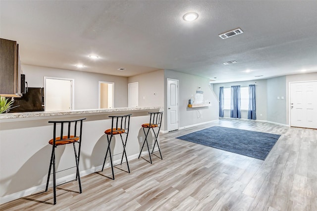 kitchen featuring light hardwood / wood-style floors, kitchen peninsula, a kitchen bar, a textured ceiling, and black refrigerator