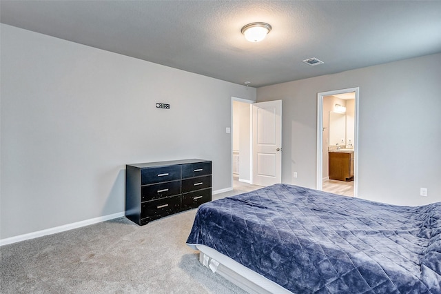 carpeted bedroom featuring a textured ceiling and ensuite bath