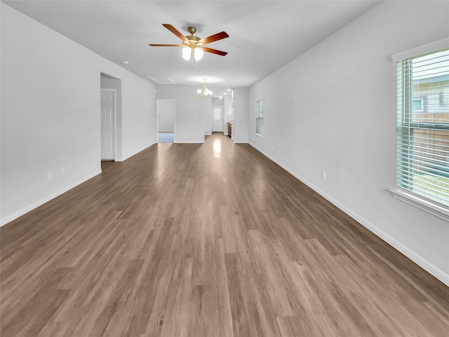 unfurnished living room with ceiling fan with notable chandelier, plenty of natural light, and dark hardwood / wood-style floors