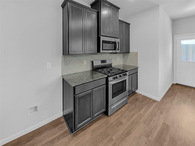 kitchen with dark stone countertops, backsplash, light hardwood / wood-style flooring, and appliances with stainless steel finishes