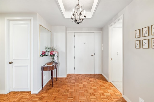 hallway with a tray ceiling, an inviting chandelier, and light parquet floors