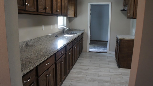 kitchen featuring dark brown cabinetry, sink, light carpet, and light stone counters