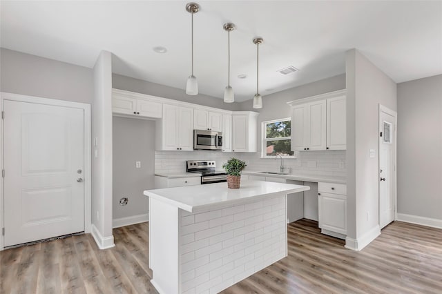 kitchen featuring sink, appliances with stainless steel finishes, decorative light fixtures, a kitchen island, and white cabinetry