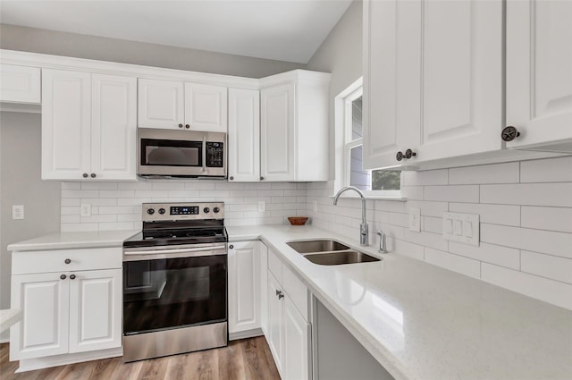 kitchen with appliances with stainless steel finishes, light stone counters, sink, light hardwood / wood-style flooring, and white cabinetry