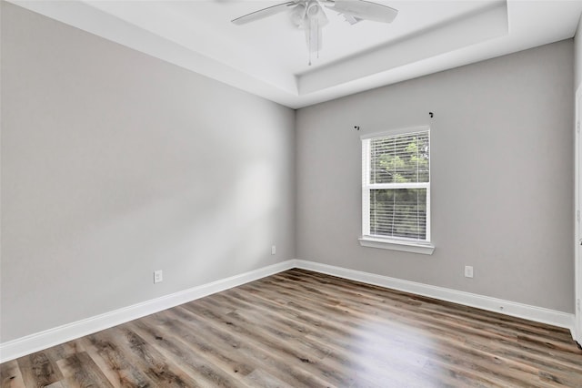 empty room with a tray ceiling, ceiling fan, and wood-type flooring