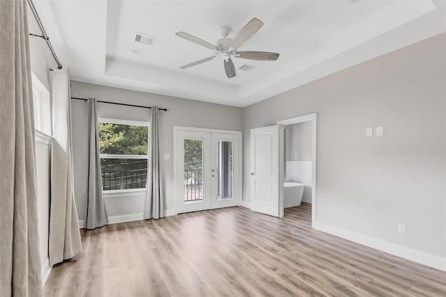 empty room with a raised ceiling, ceiling fan, french doors, and light wood-type flooring