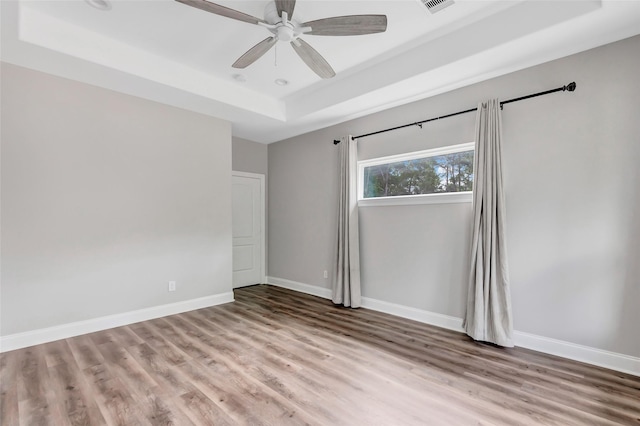 empty room featuring a tray ceiling, ceiling fan, and light wood-type flooring