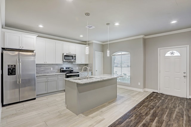 kitchen with hanging light fixtures, decorative backsplash, crown molding, appliances with stainless steel finishes, and a kitchen island with sink