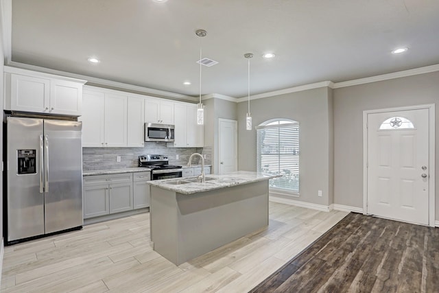 kitchen with sink, a center island with sink, pendant lighting, stainless steel appliances, and light stone countertops