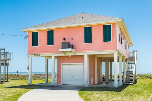 view of front of house with central AC unit, a water view, a garage, and a front lawn