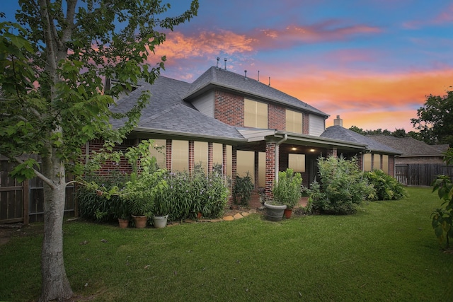 back house at dusk featuring a lawn