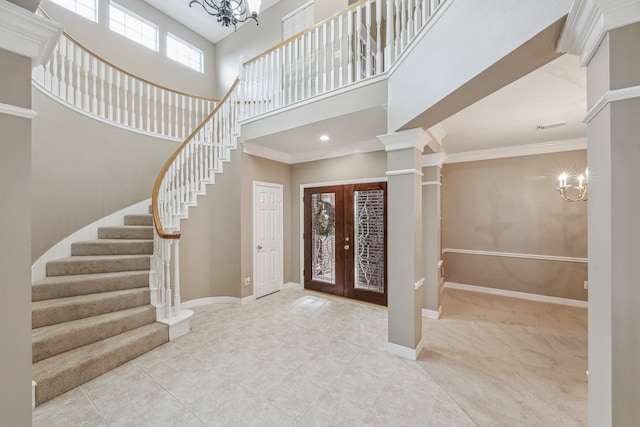 entrance foyer with ornate columns, a high ceiling, french doors, ornamental molding, and a notable chandelier