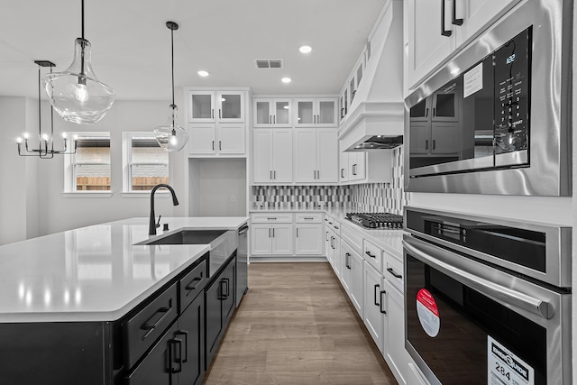 kitchen with white cabinetry, hanging light fixtures, stainless steel appliances, an island with sink, and light hardwood / wood-style floors