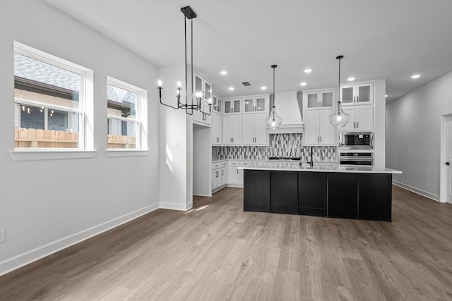 kitchen featuring white cabinetry, backsplash, decorative light fixtures, a center island with sink, and appliances with stainless steel finishes