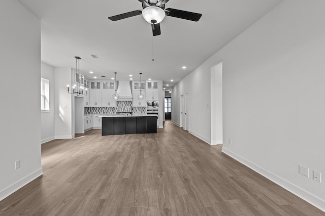 kitchen featuring custom range hood, a kitchen island, hanging light fixtures, white cabinetry, and stainless steel microwave