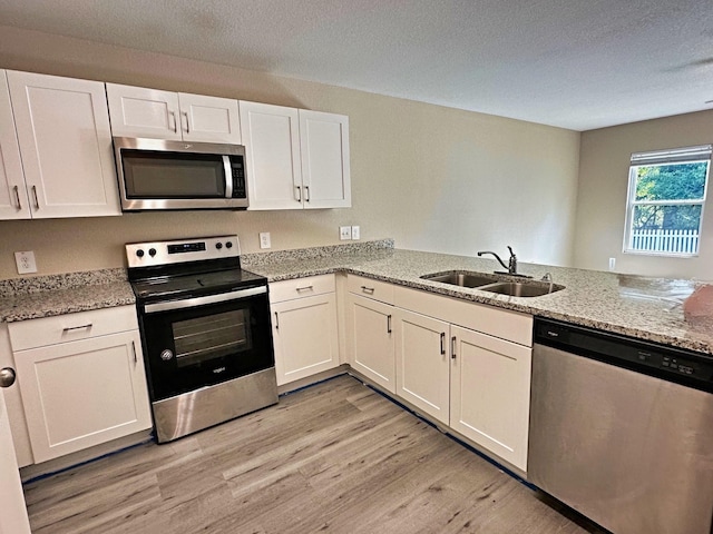 kitchen with sink, appliances with stainless steel finishes, kitchen peninsula, light stone countertops, and white cabinets