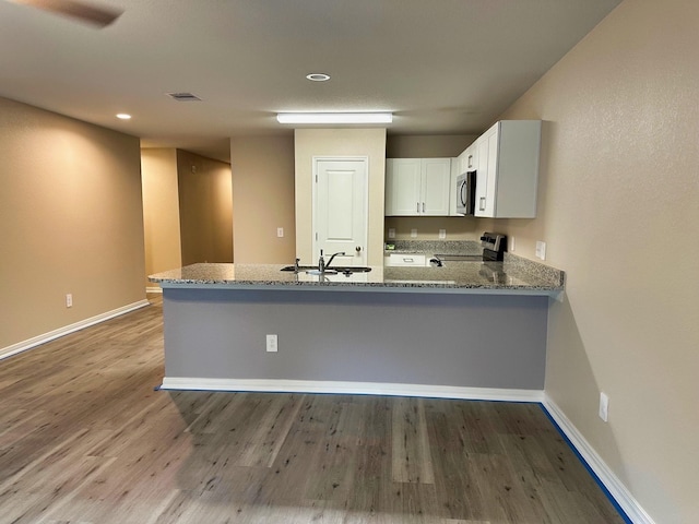 kitchen with sink, kitchen peninsula, stainless steel appliances, light stone countertops, and white cabinets