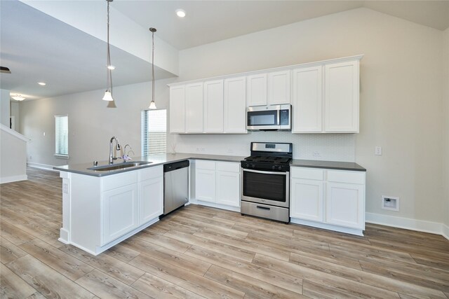 kitchen featuring kitchen peninsula, appliances with stainless steel finishes, sink, decorative light fixtures, and white cabinetry