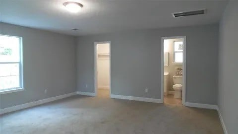 unfurnished bedroom featuring a closet, carpet, ensuite bathroom, and a walk in closet