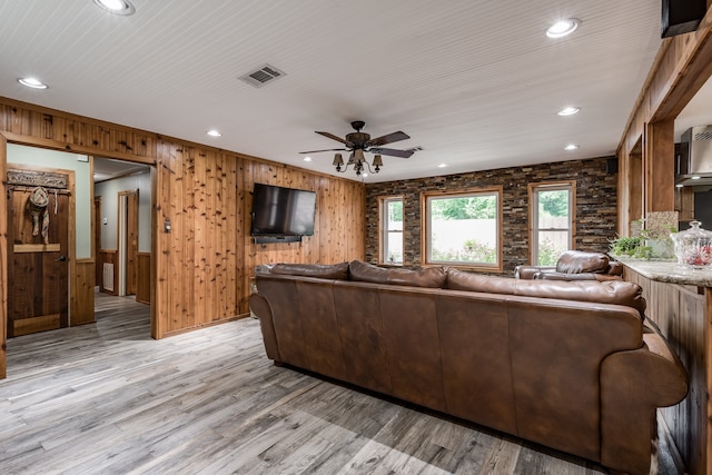 living room with light hardwood / wood-style floors, wood walls, and ceiling fan