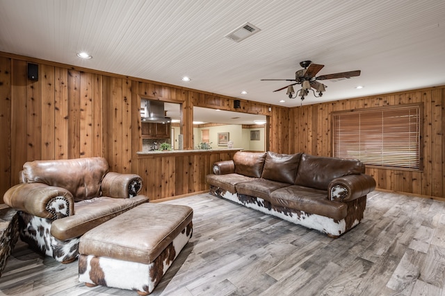 living room with hardwood / wood-style flooring, wooden walls, and ceiling fan