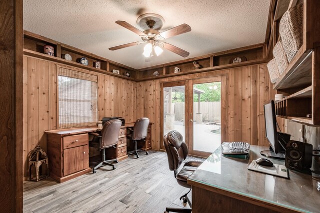 office area featuring french doors, light wood-type flooring, a textured ceiling, wood walls, and ceiling fan