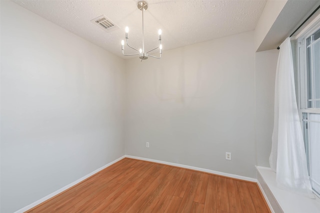 spare room with light wood-style flooring, visible vents, a chandelier, and baseboards