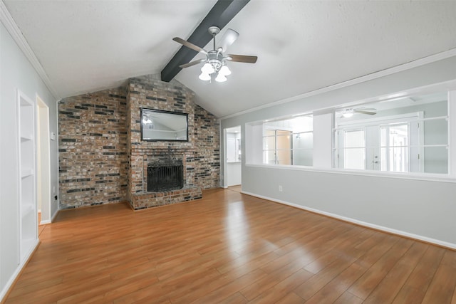 unfurnished living room featuring a ceiling fan, a brick fireplace, lofted ceiling with beams, and wood finished floors