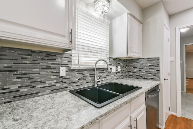 kitchen with wood finished floors, a sink, white cabinetry, stainless steel dishwasher, and backsplash