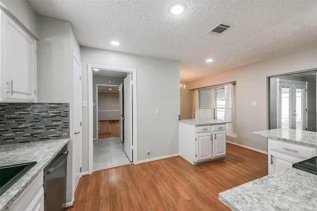 kitchen with backsplash, visible vents, light wood-style flooring, and stainless steel dishwasher