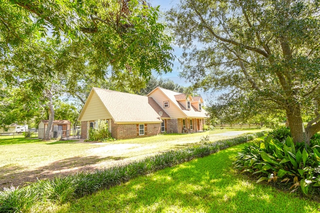 view of side of home featuring fence, driveway, a shingled roof, a lawn, and brick siding