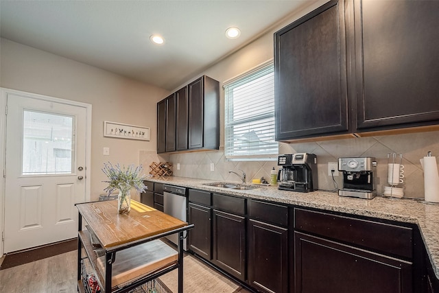 kitchen with dark brown cabinetry, sink, light stone counters, decorative backsplash, and light wood-type flooring