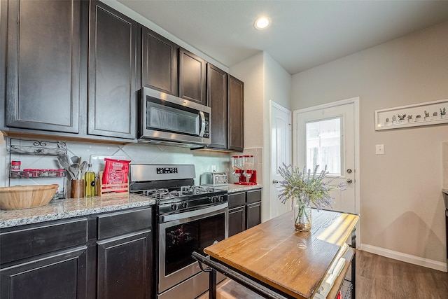 kitchen with dark brown cabinetry, light stone countertops, stainless steel appliances, tasteful backsplash, and dark hardwood / wood-style floors