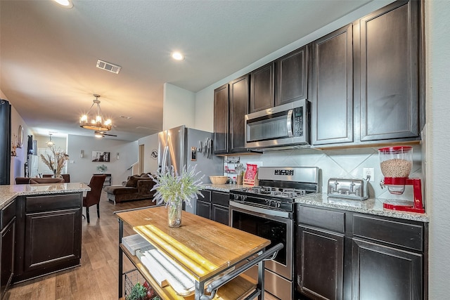 kitchen with light stone counters, light hardwood / wood-style flooring, stainless steel appliances, and an inviting chandelier