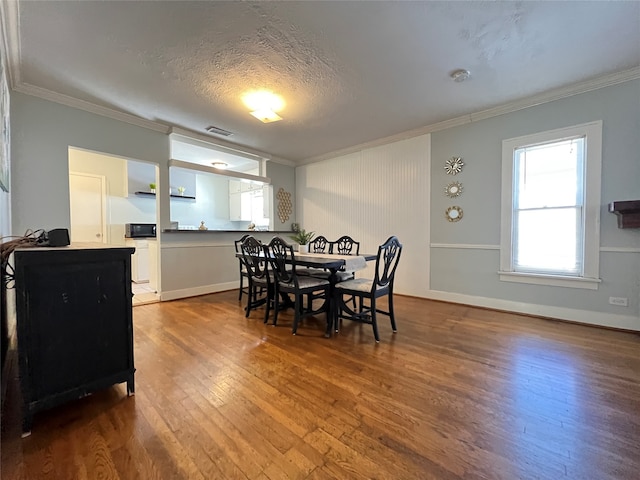 dining space featuring ornamental molding, wood-type flooring, and a textured ceiling