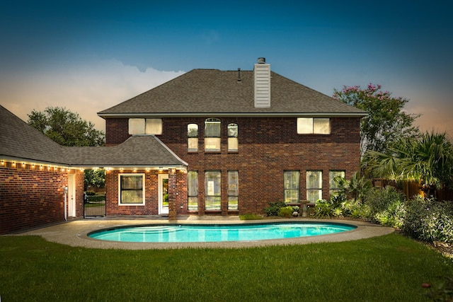 rear view of house with an outdoor pool, a lawn, a chimney, roof with shingles, and brick siding