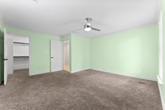 unfurnished bedroom with carpet floors, crown molding, a spacious closet, ceiling fan, and baseboards