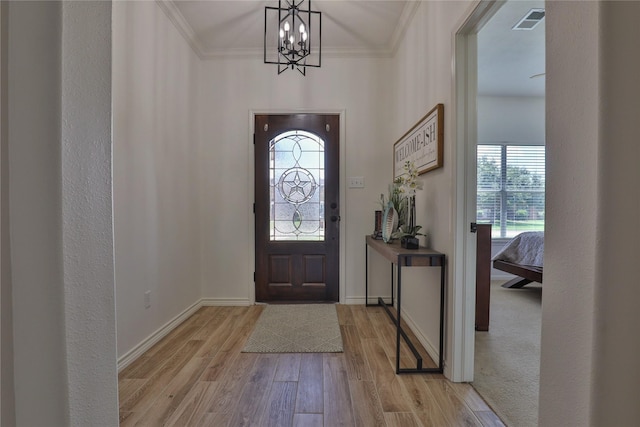 foyer entrance with light wood-type flooring, ornamental molding, and a notable chandelier