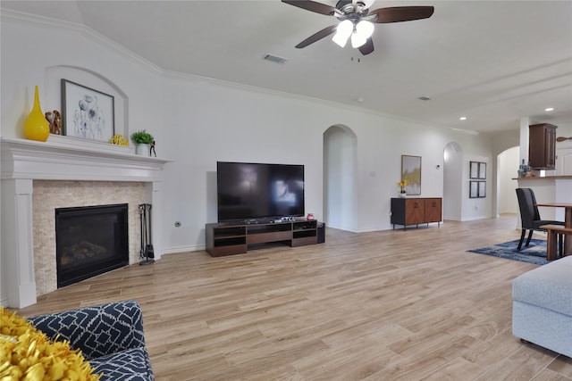 living room with a fireplace, ornamental molding, ceiling fan, and light wood-type flooring