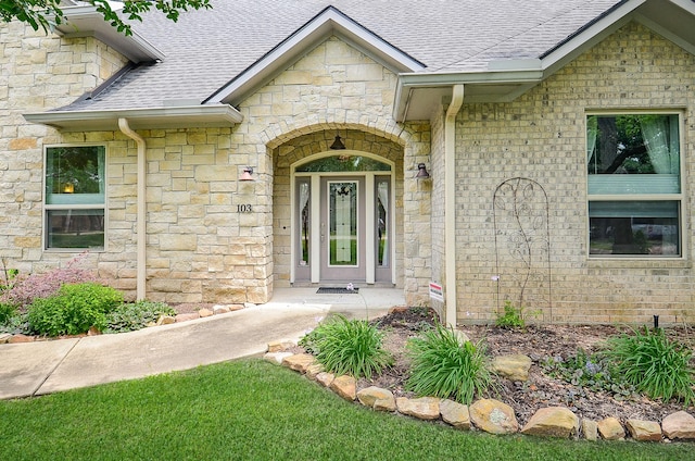 entrance to property featuring stone siding and a shingled roof