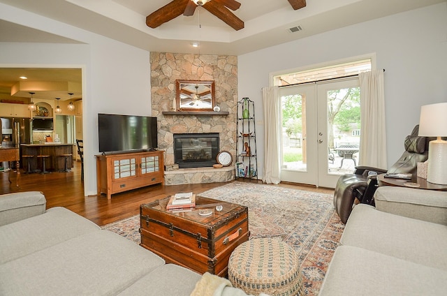 living room with ceiling fan, a stone fireplace, french doors, wood finished floors, and a raised ceiling