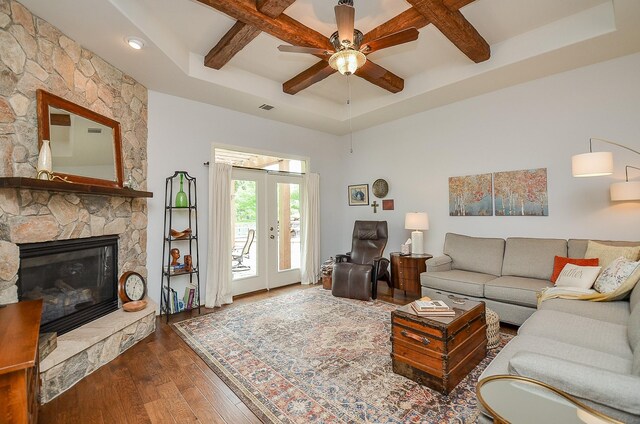 living room featuring coffered ceiling, a stone fireplace, dark wood-type flooring, and ceiling fan