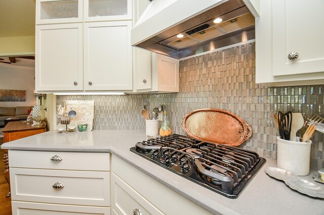 kitchen with white cabinetry, black gas stovetop, custom range hood, and tasteful backsplash