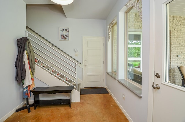 foyer entrance featuring stairway, finished concrete flooring, and baseboards