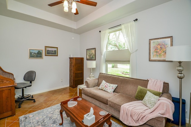 living room with tile patterned flooring, a tray ceiling, baseboards, and ceiling fan