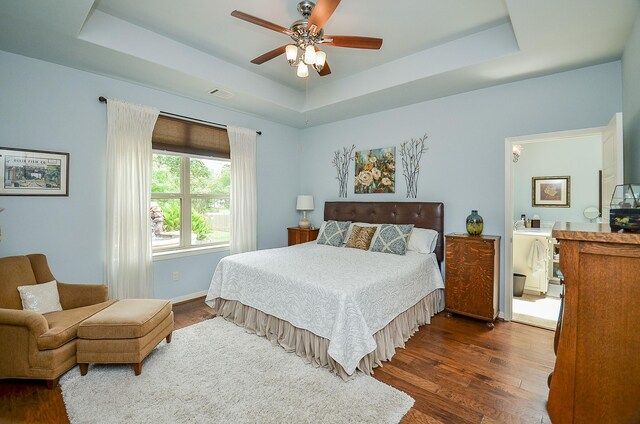 bedroom with dark hardwood / wood-style floors, ceiling fan, and a tray ceiling