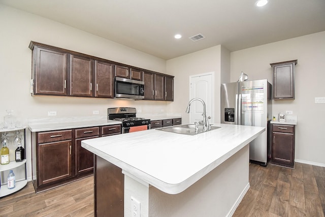 kitchen featuring a kitchen island with sink, sink, dark hardwood / wood-style floors, appliances with stainless steel finishes, and dark brown cabinetry