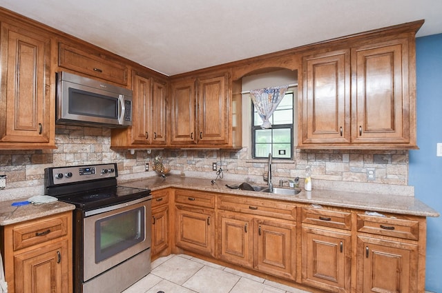 kitchen with sink, decorative backsplash, light stone countertops, appliances with stainless steel finishes, and light tile patterned flooring