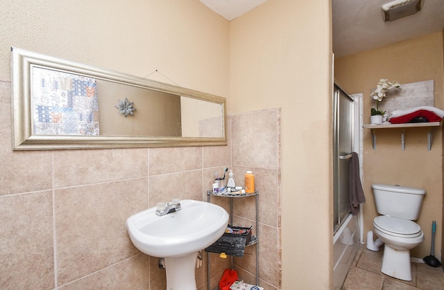 full bathroom with tile patterned floors, toilet, enclosed tub / shower combo, and tile walls